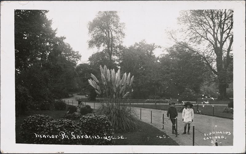 A view of shrubs and trees in Manor House Gardens with two children standing beside railings in the foreground.